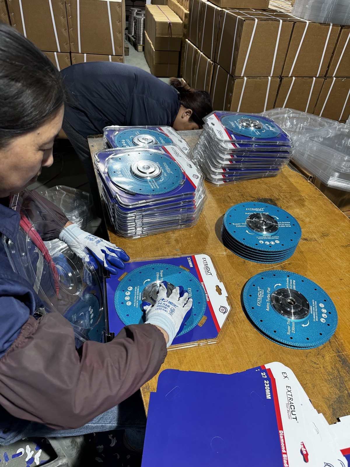 Workers blister-packing blue EXTRACUT diamond saw blades at the packing table